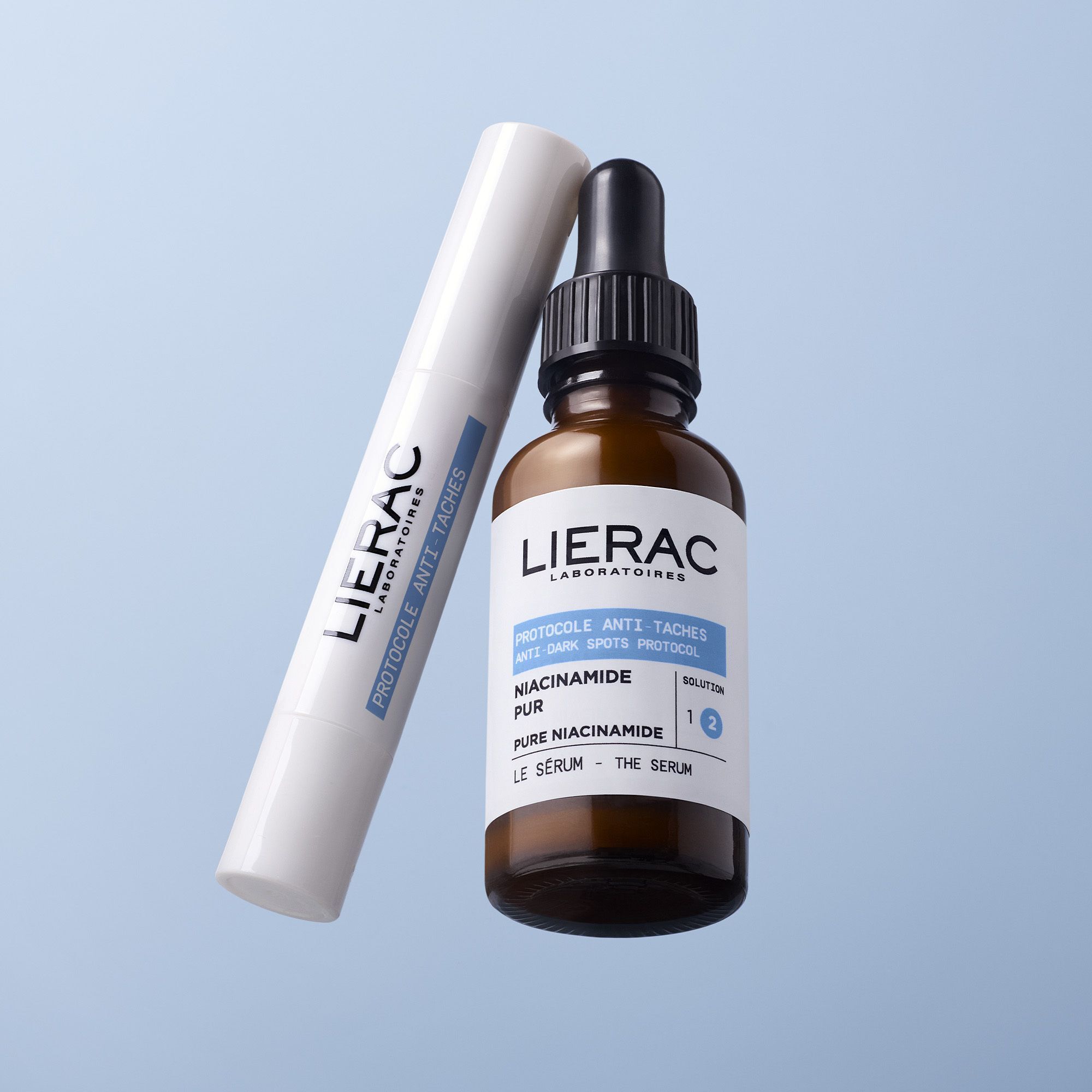 Lierac Anti-Taches serumflesje en pen, op blauwe achtergrond.