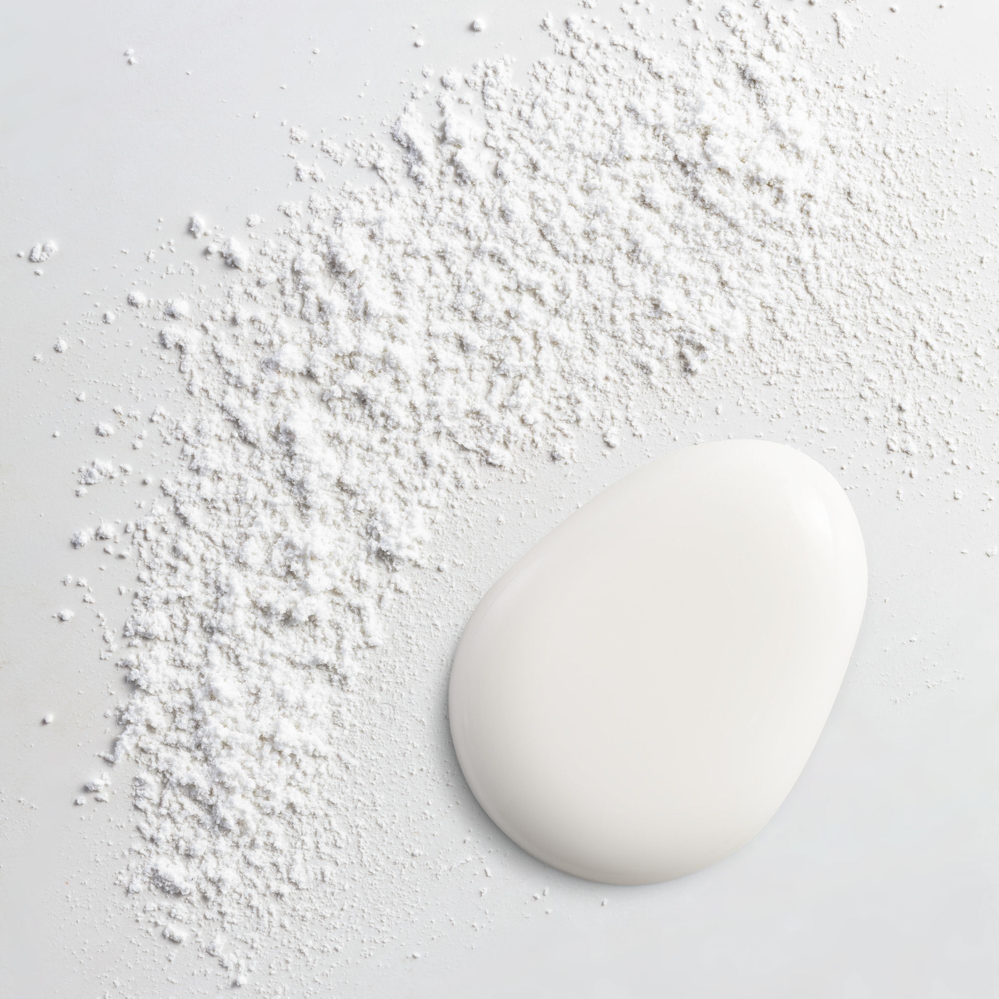 Une goutte liquide blanche à côté d'une traînée de poudre blanche sur fond blanc.