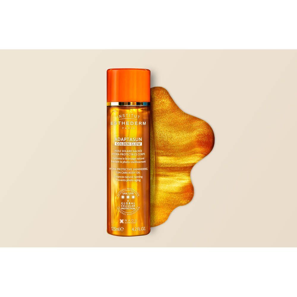 Flacon d'Huile Solaire Nacrée Hydra-Protectrice Corps Institut Esthederm Golden Glow à côté d'un objet doré et scintillant.