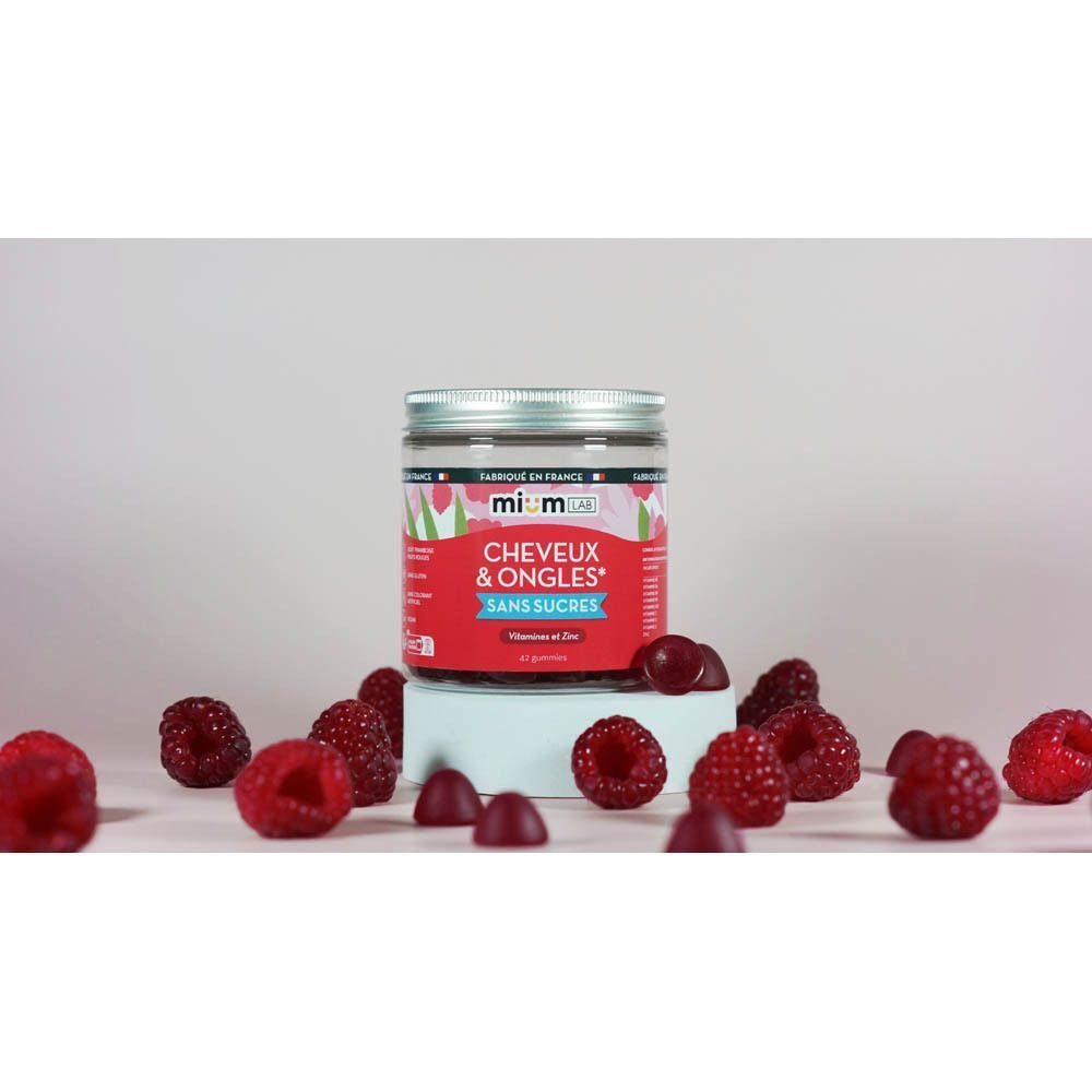 Gummies MiumLab Cheveux & Ongles sur un socle, entourés de framboises.