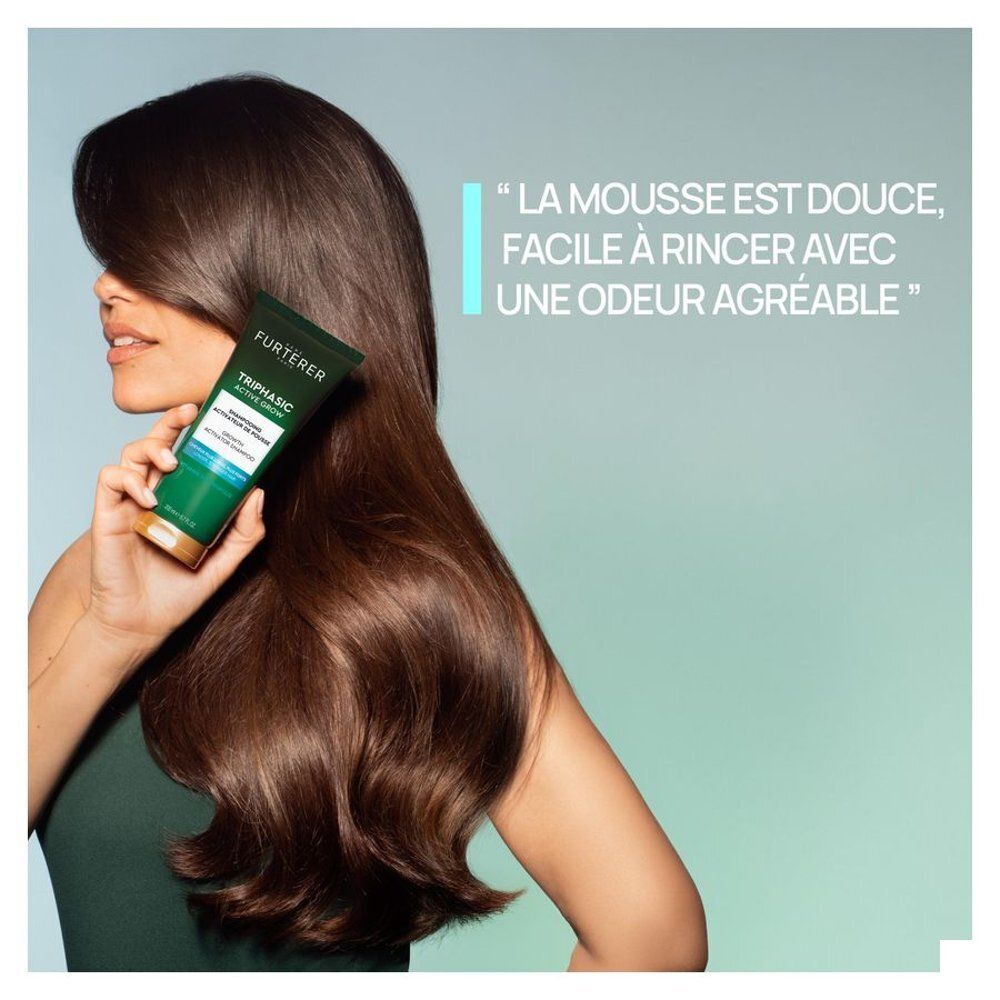Femme tenant un flacon de shampooing René Furterer Triphasic Active Grow à côté de ses longs cheveux.