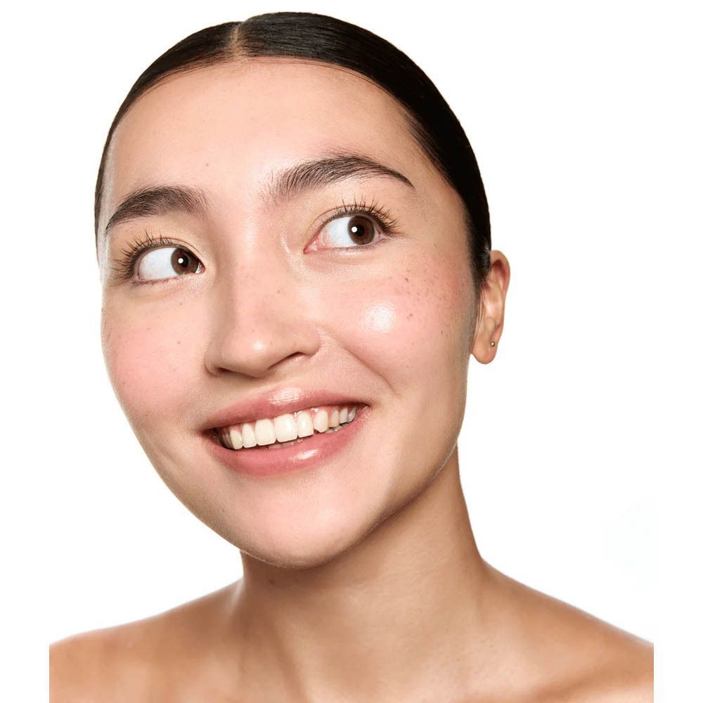 Gros plan d'un visage souriant, peau radieuse, regard tourné vers le haut.