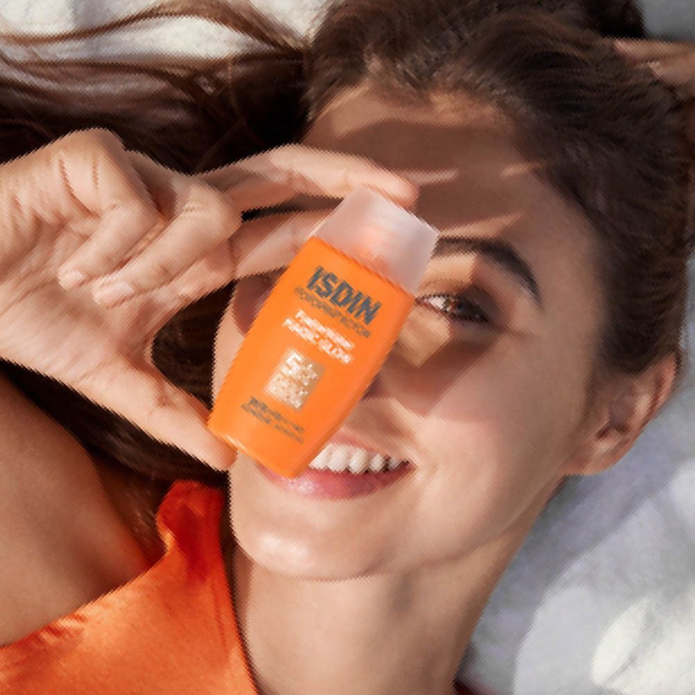 Une femme tient un flacon d'ISDIN Fusion Water Magic Glow SPF50 devant son visage, souriante.