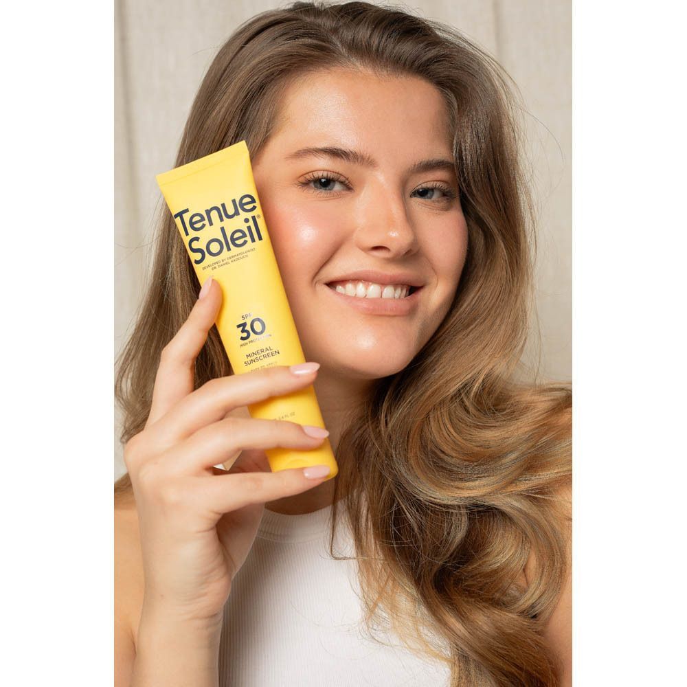 Une femme tient un tube jaune de crème solaire minérale Tenue Soleil SPF 30.