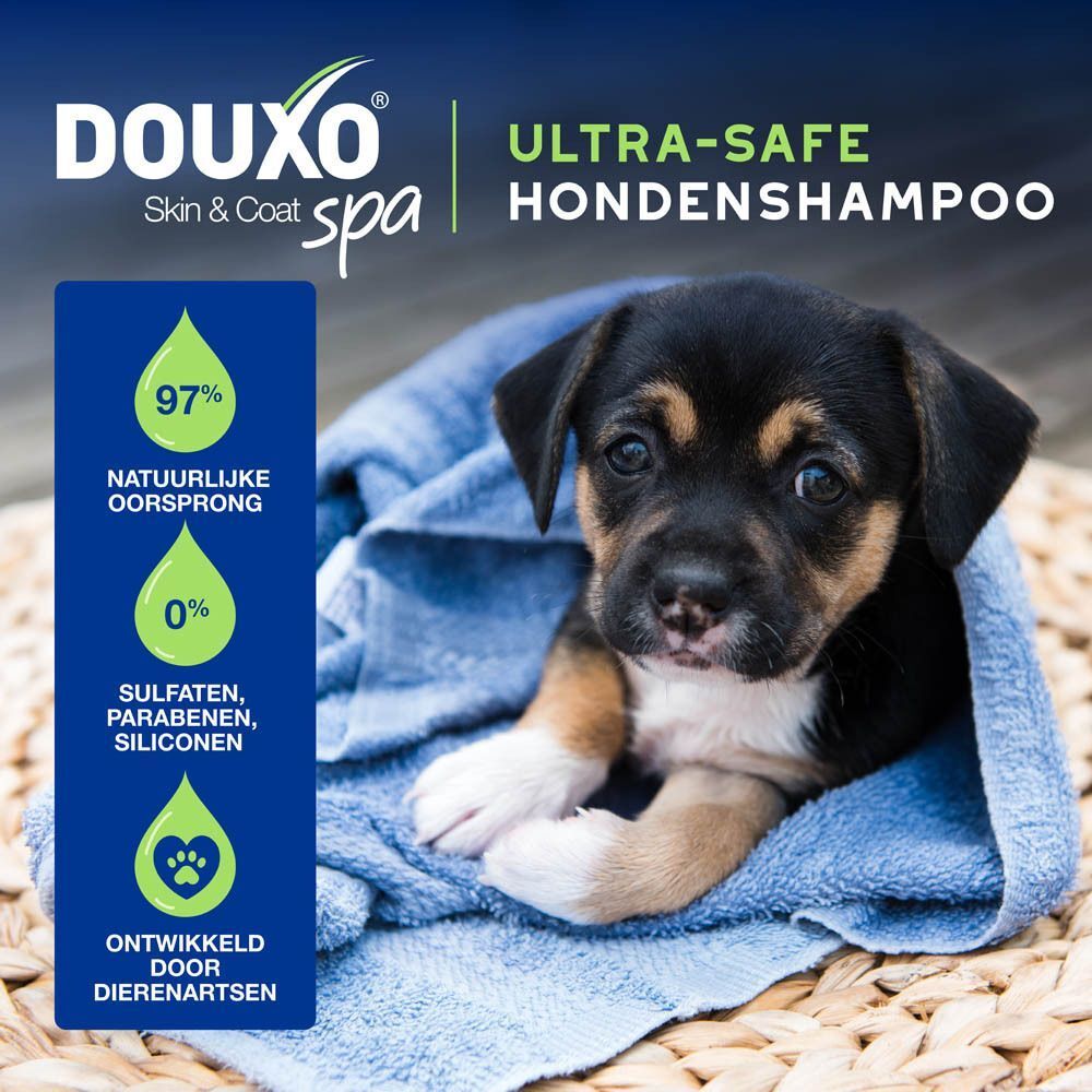 Een puppy, gewikkeld in een handdoek, met informatie over Douxo Spa shampoo.