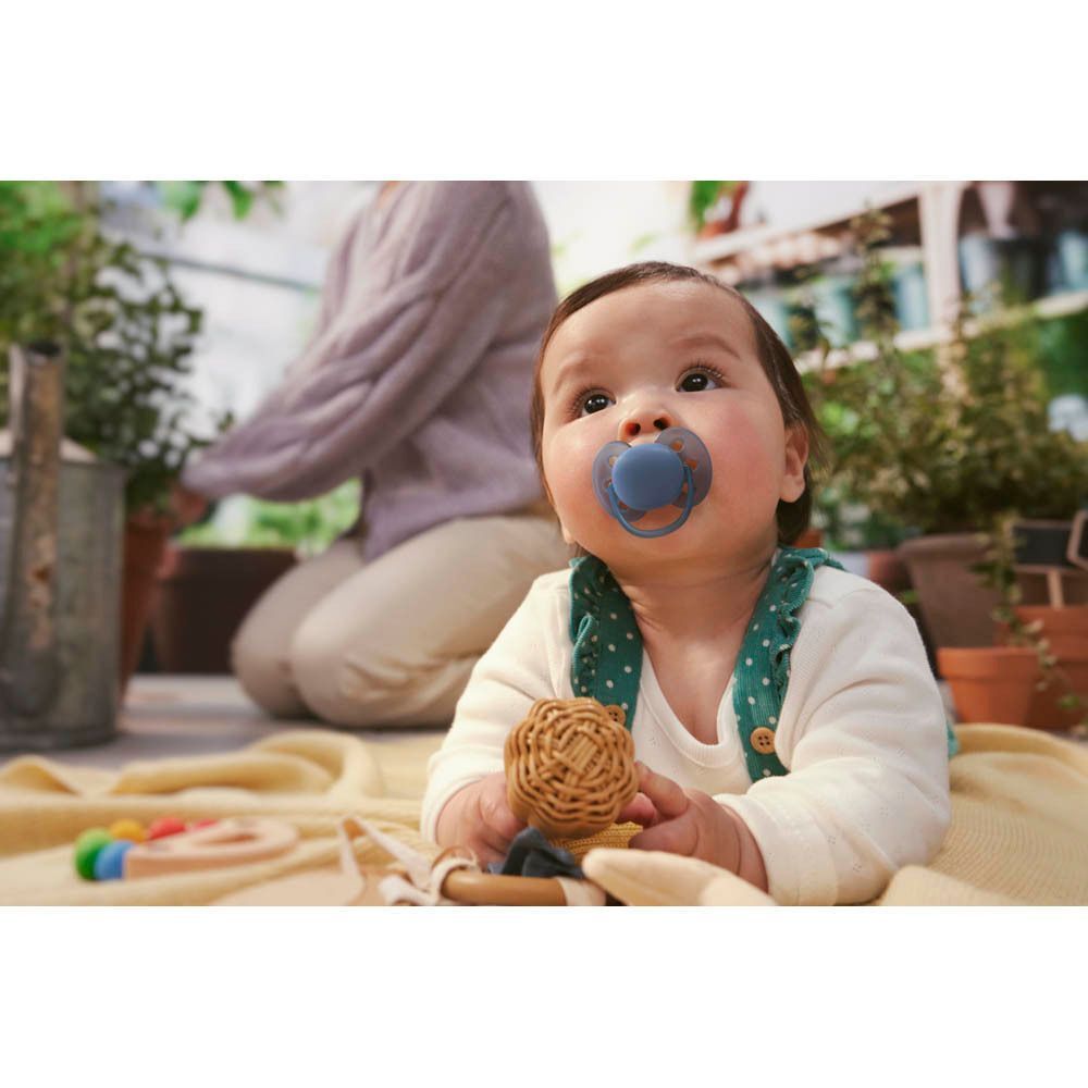 Un bébé avec une sucette Philips Avent bleu clair dans la bouche, allongé sur une couverture.