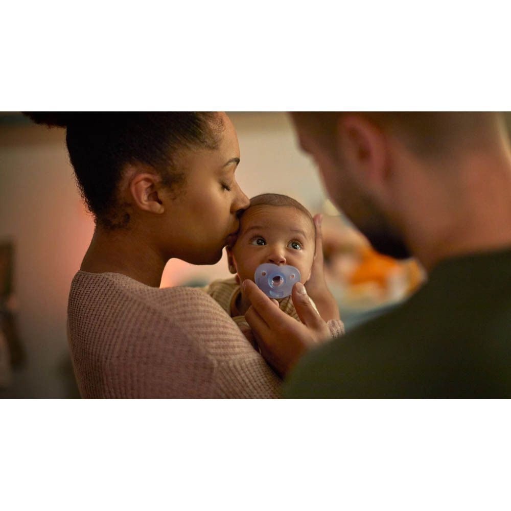 Een baby met een blauwe Philips Avent Soothie fopspeen in de mond, vastgehouden door ouders.