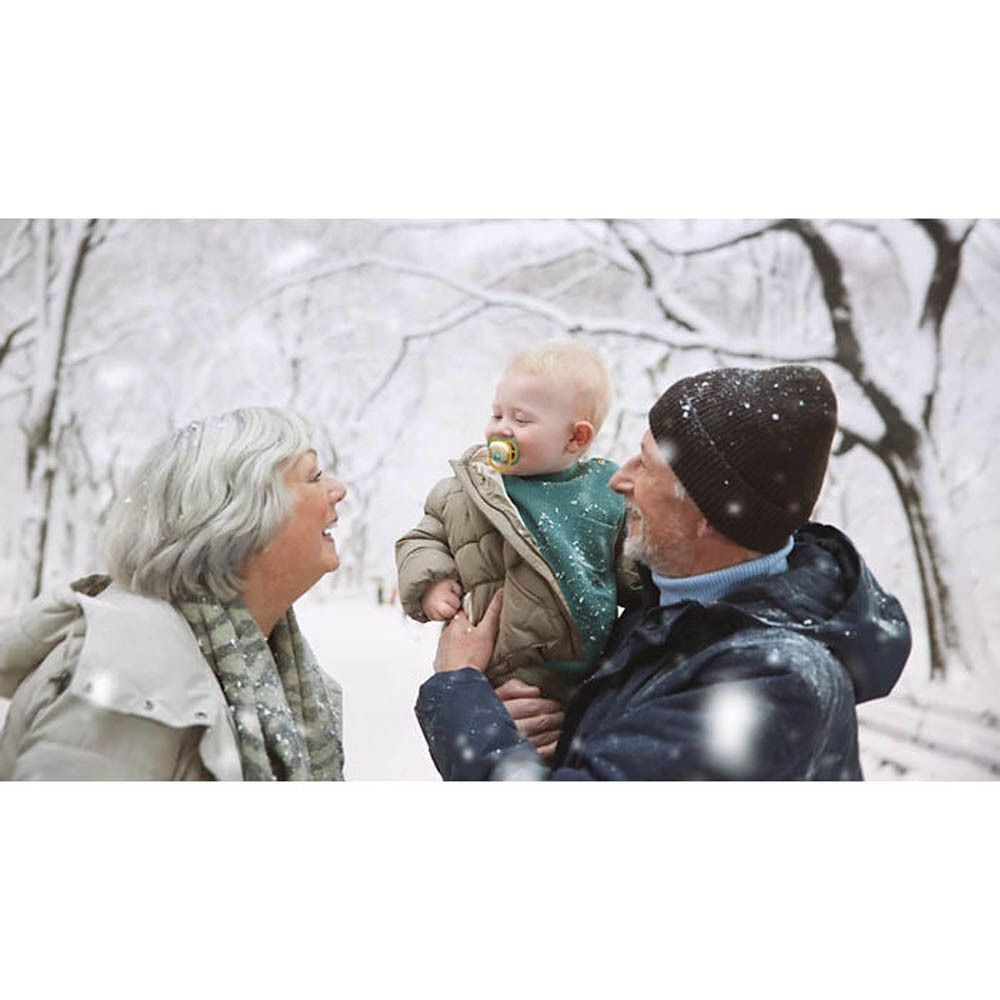 Un bébé avec une sucette Philips Avent dans la neige, tenu par ses grands-parents.