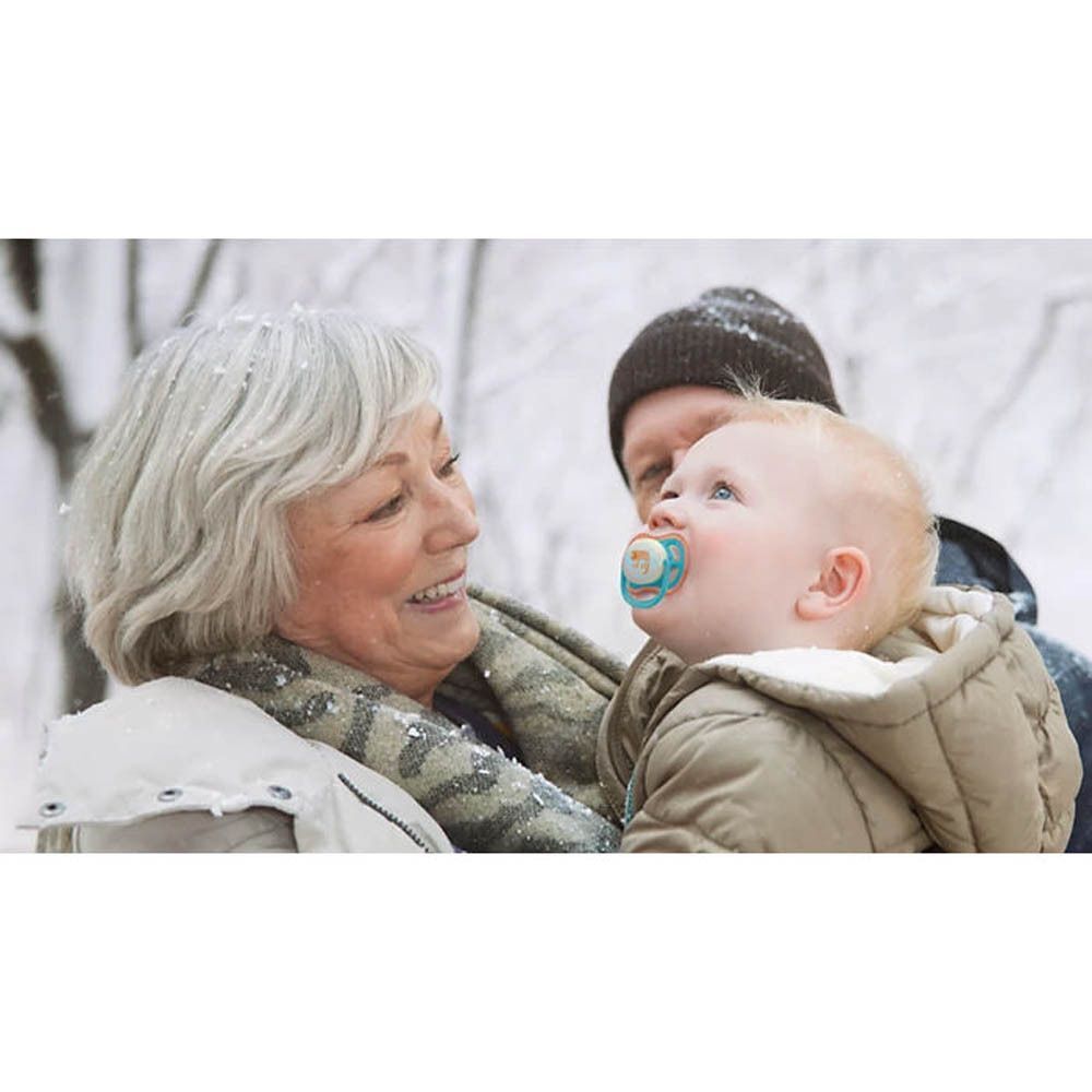 Un bébé avec une sucette Philips Avent dans les bras de sa grand-mère dans la neige.