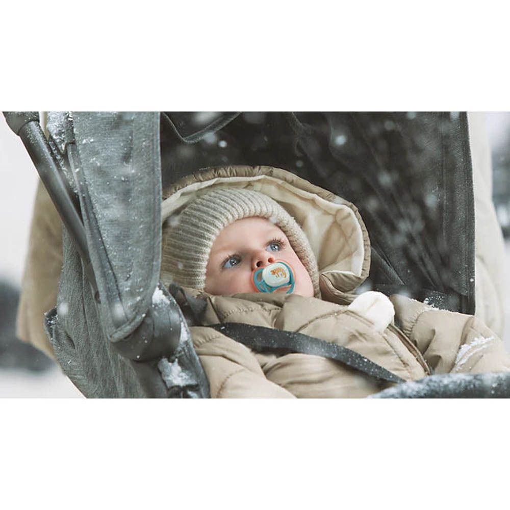 Un bébé dans une poussette avec une sucette Philips Avent dans la neige.