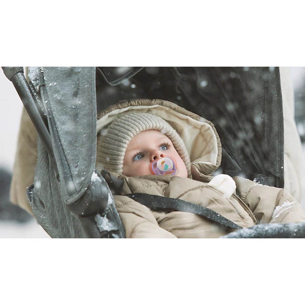 Bébé avec sucette Philips Avent dans une poussette sous la neige.