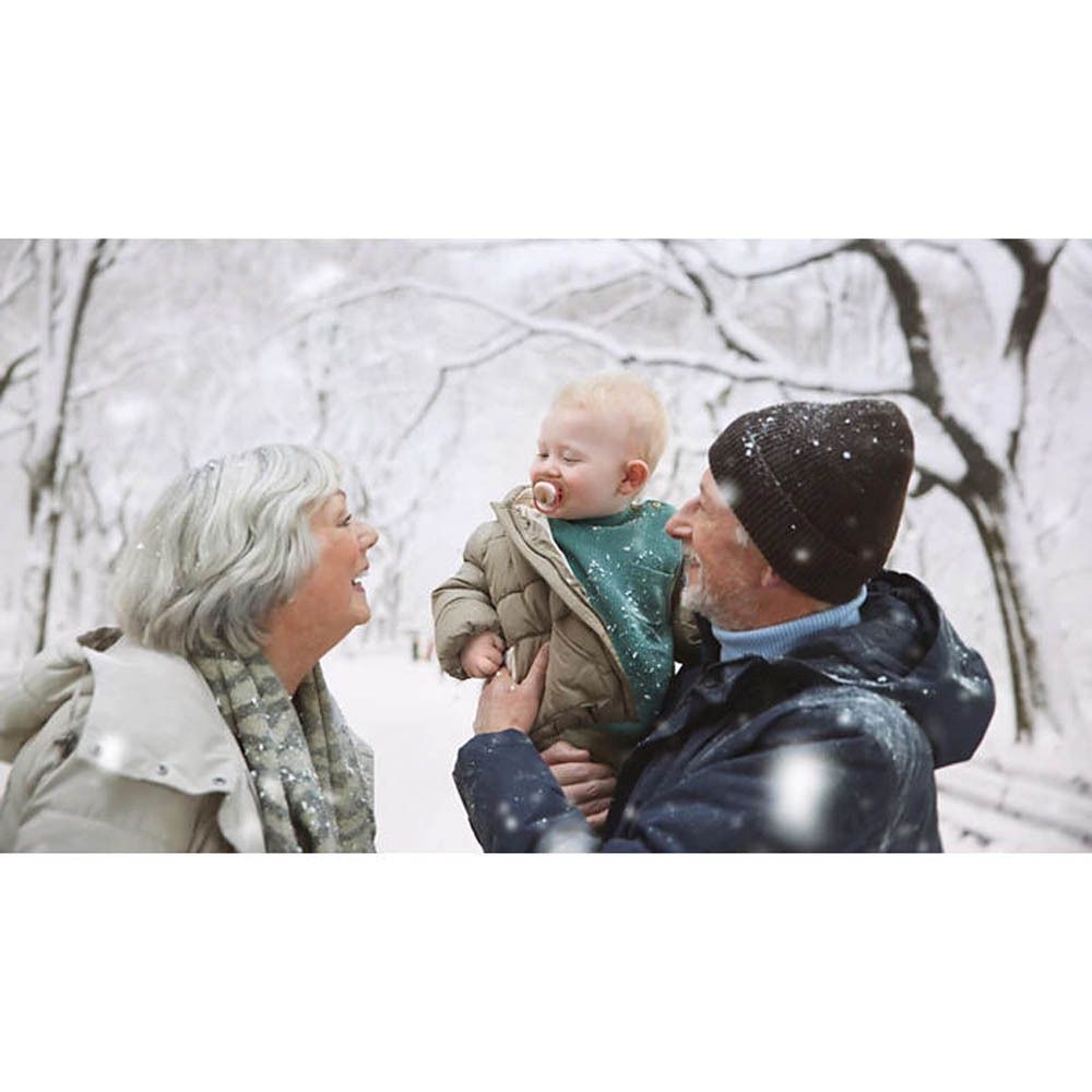 Bébé avec sucette dans les bras du grand-père sous la neige. Grand-mère sourit.