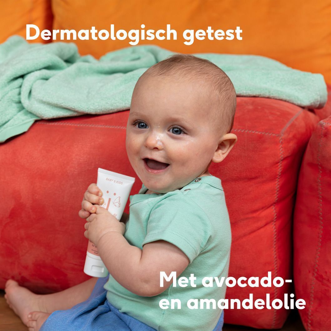 Baby zit op de grond en houdt een tube Naïf crème vast, met Vegan-keurmerk.