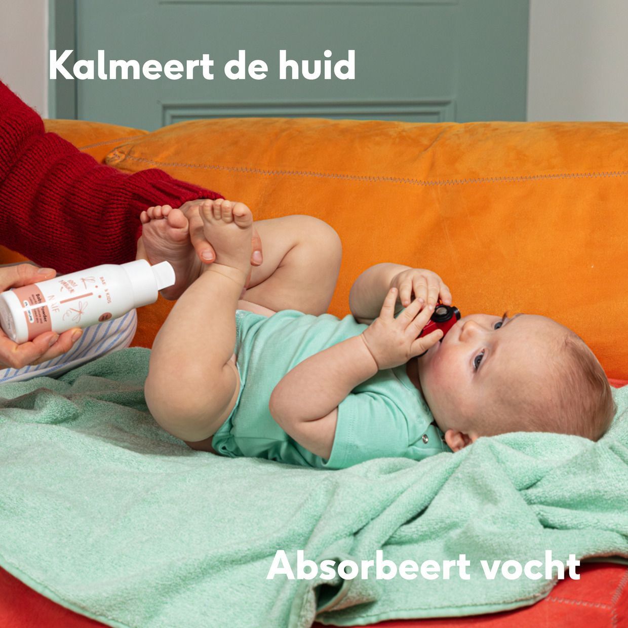 Baby ligt op een deken, hand houdt babypoederfles vast.