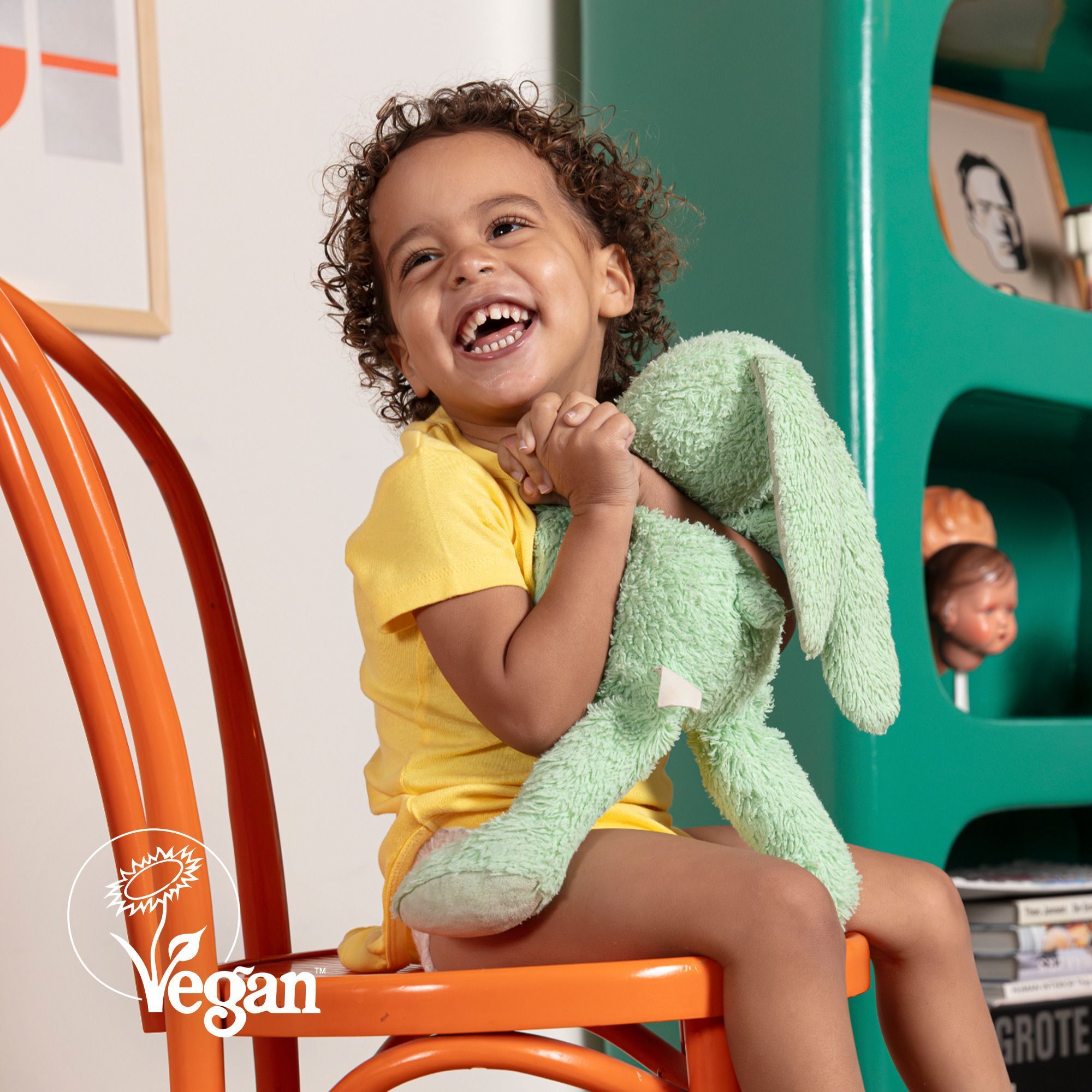 Un enfant souriant tenant un lapin en peluche vert, logo Vegan visible.