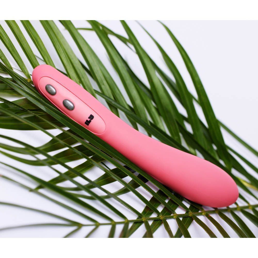 Un vibromasseur rose incurvé posé sur des feuilles vertes.