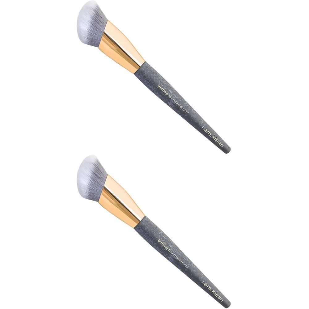 Deux pinceaux de fond de teint avec manche gris, virole dorée et tête de brosse blanche.