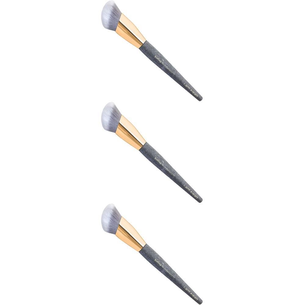 Trois pinceaux de fond de teint avec des poils gris, un collier doré et un manche texturé foncé.