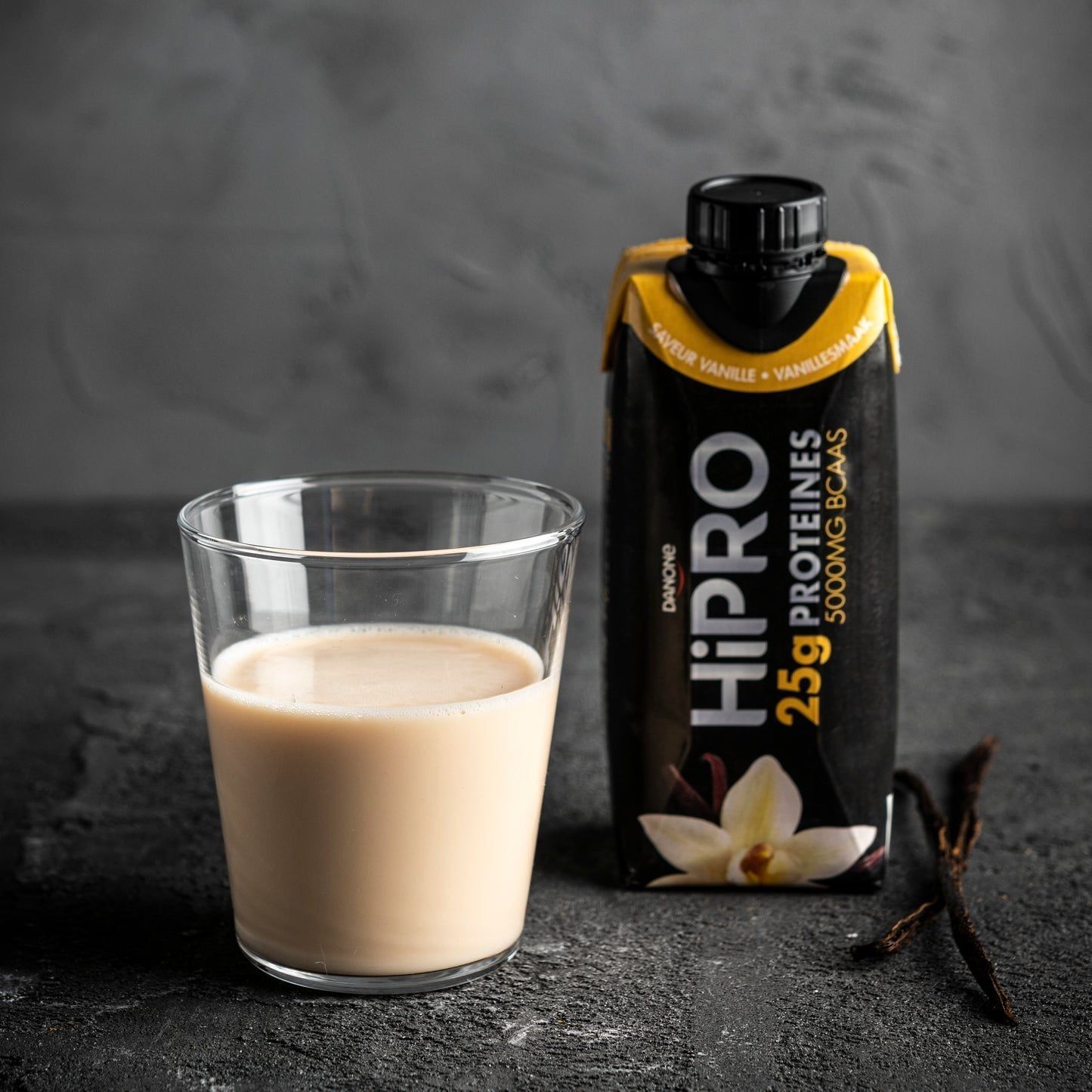 Boisson Danone HiPRO Vanille à côté d'un verre de lait. Avec fleur et gousses de vanille.