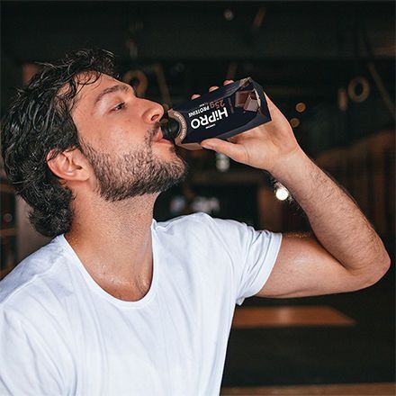 Homme buvant une boisson Danone HiPRO Chocolat dans une salle de sport.