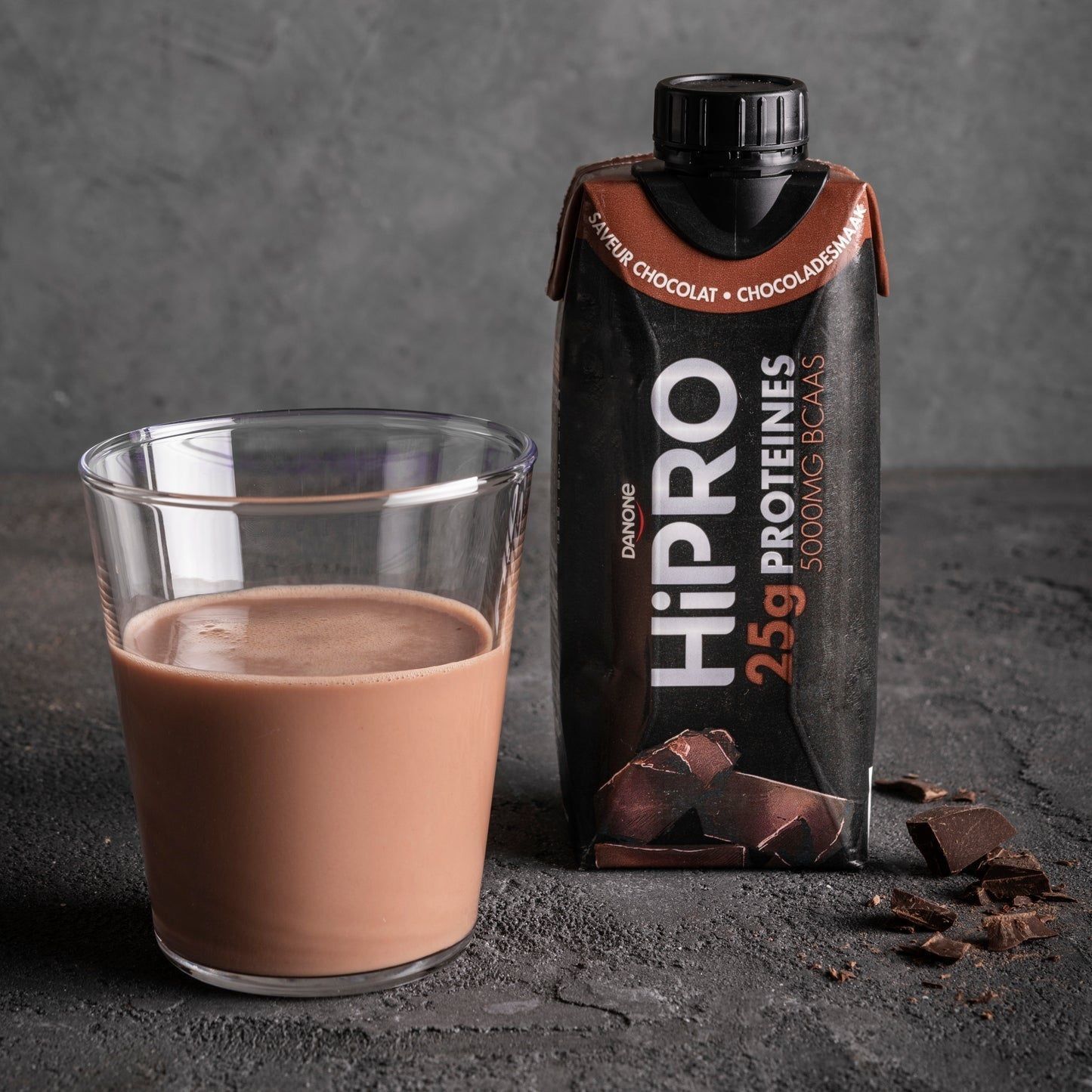 Boisson Danone HiPRO Chocolat à côté d'un verre de chocolat au lait et de morceaux de chocolat.