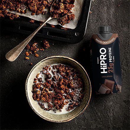 Boisson Danone HiPRO Chocolat à côté d'un bol de muesli avec du lait et des morceaux de chocolat.