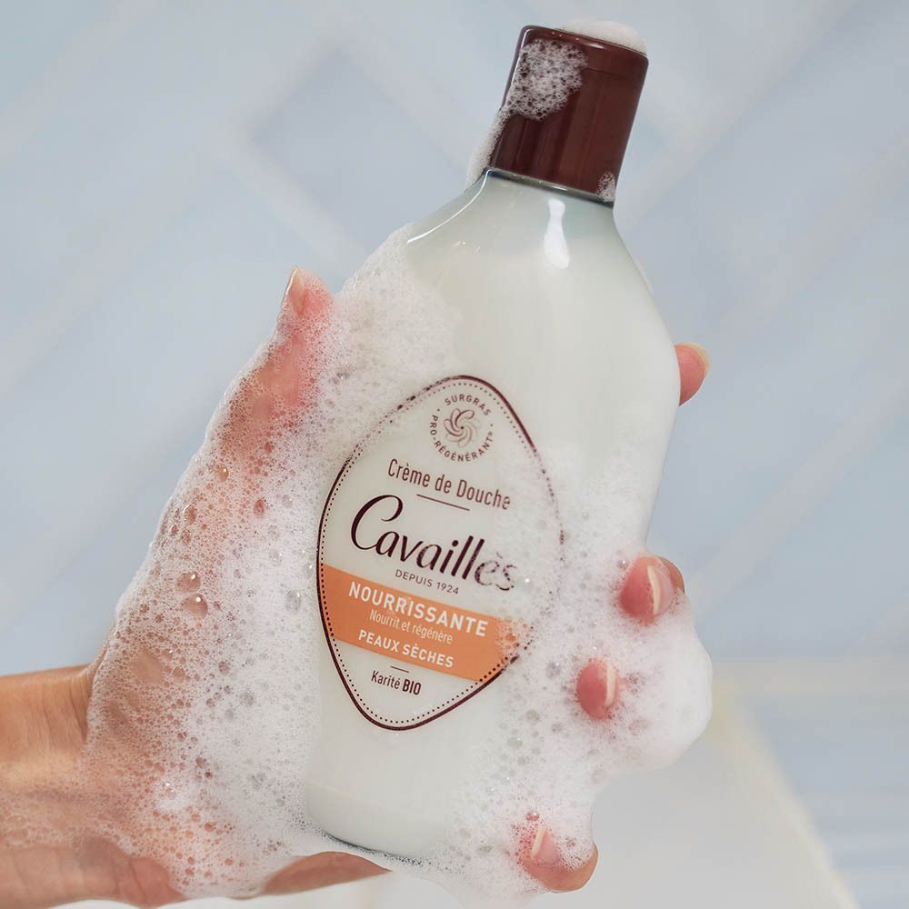 Une main tenant un flacon de Crème de Douche Roge Cavailles couvert de mousse.