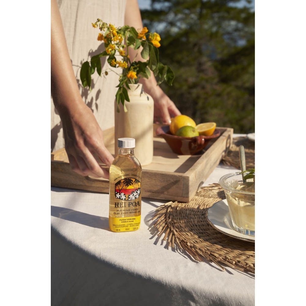 Een fles HEI POA Monoi olie vanillegeur op een buitentafel.