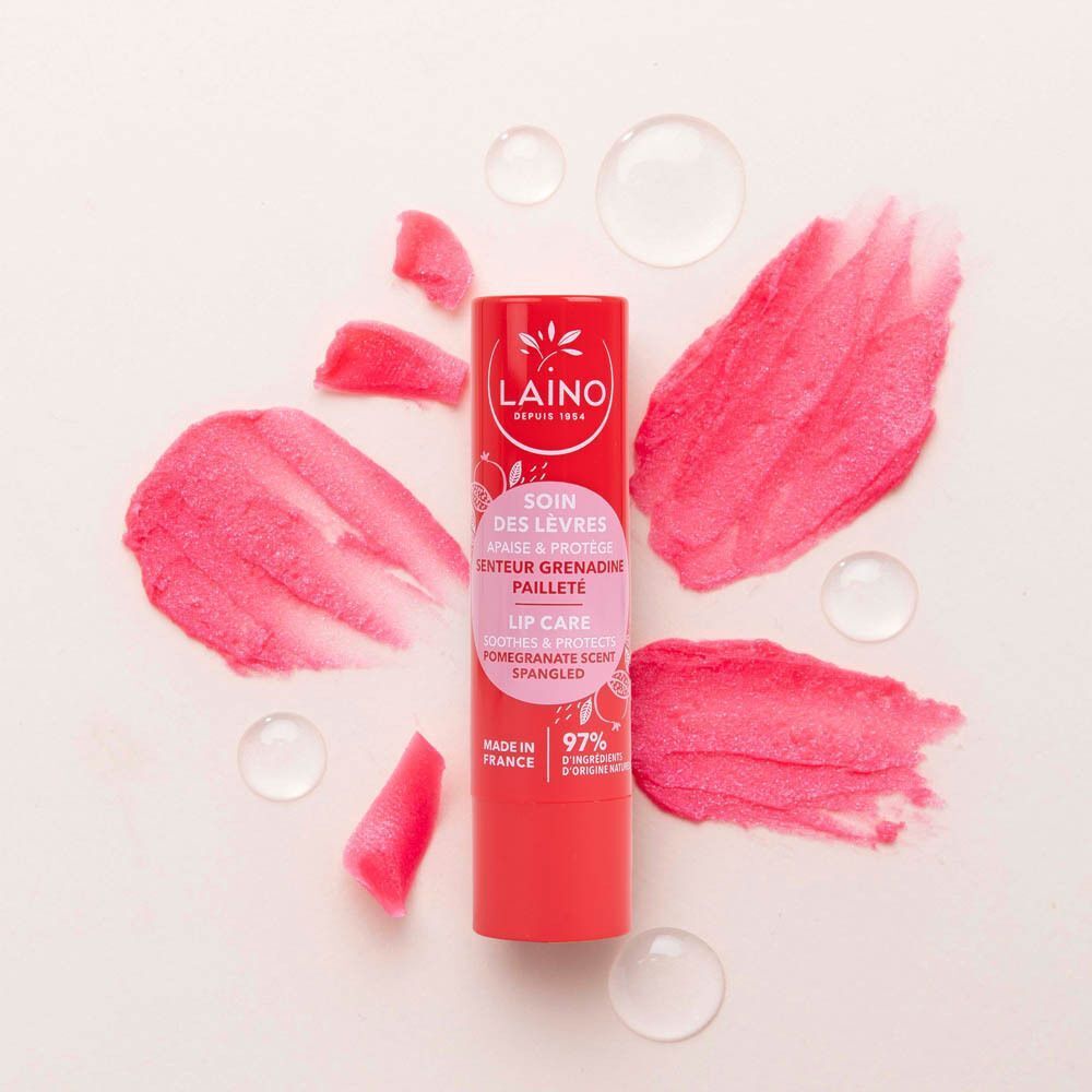 Un baume à lèvres rouge entouré de texture grenade et de gouttes d'eau.