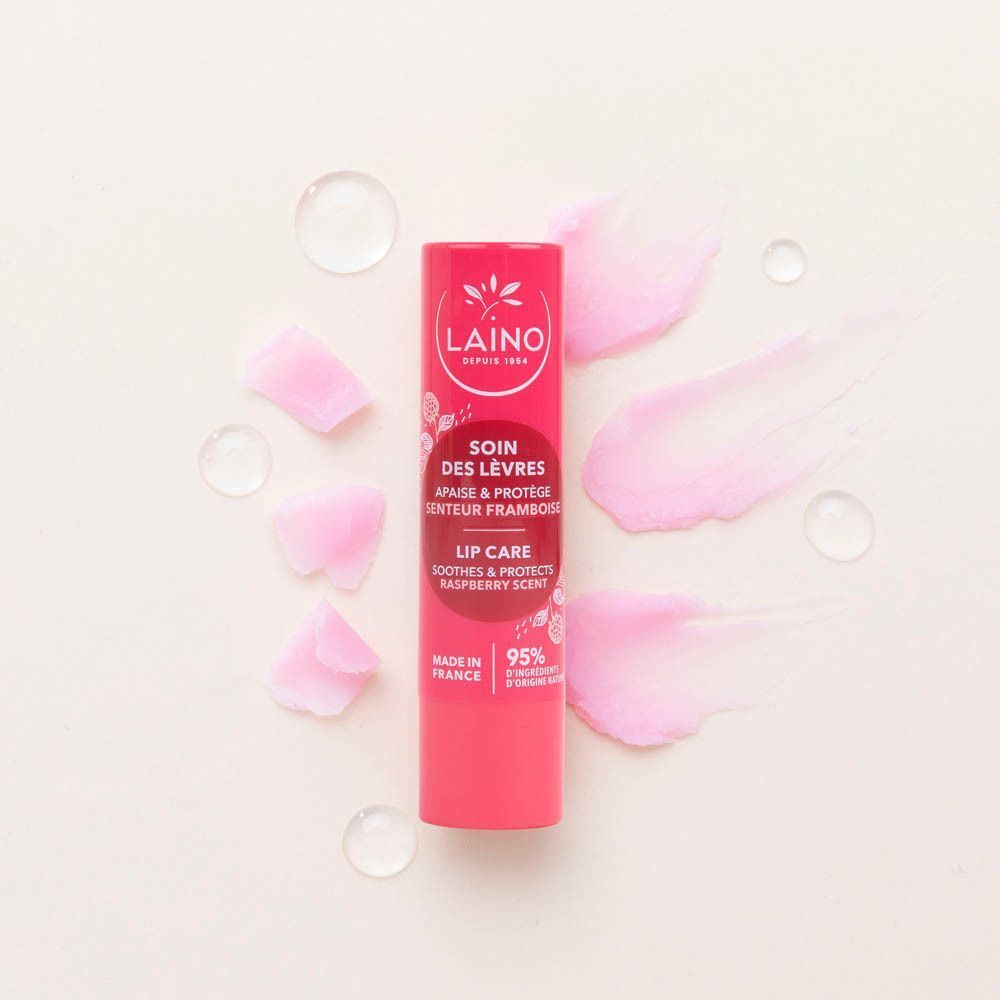 Een Laino lippenbalsemstick met frambozengeur, omringd door bloemblaadjes en waterdruppels.