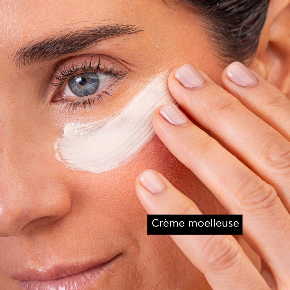 Une femme appliquant le masque pour les yeux Apivita Express Beauty à l'extrait de raisin.