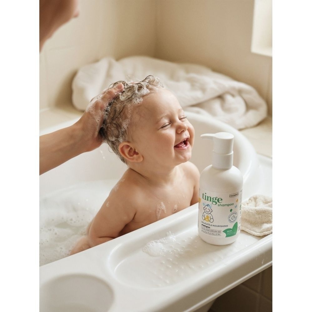 Un flacon blanc de shampooing pour bébé Tinge avec distributeur à pompe, entouré de mousse sur une surface en marbre.
