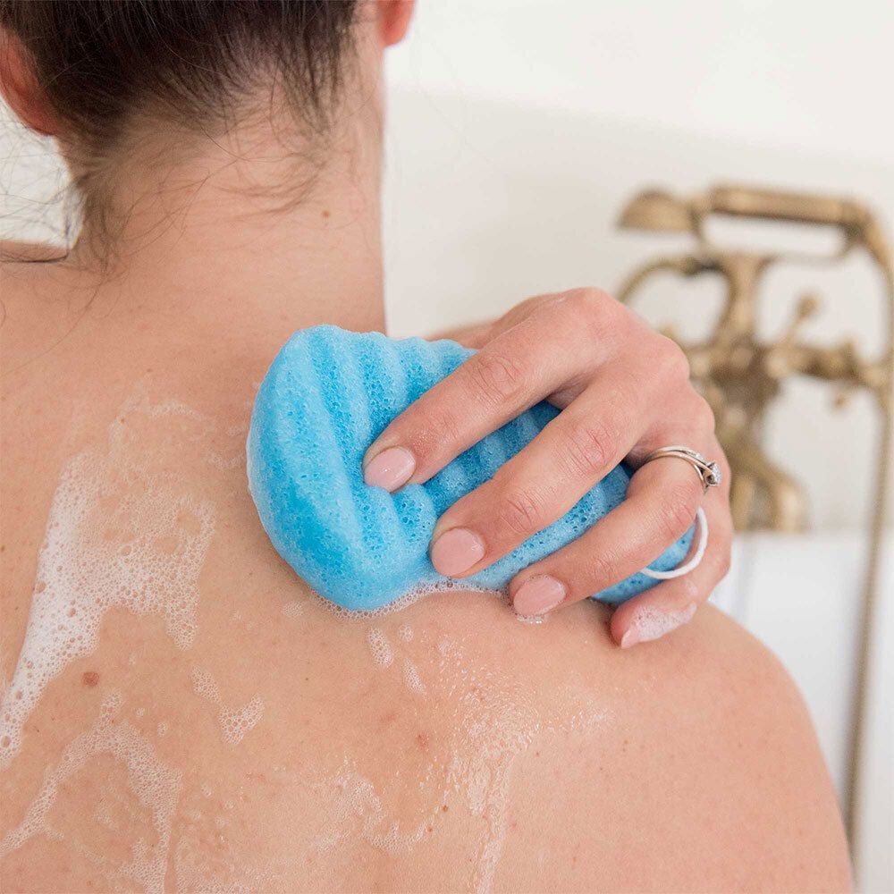 Main utilisant une éponge Konjac bleue pour un massage doux du dos.