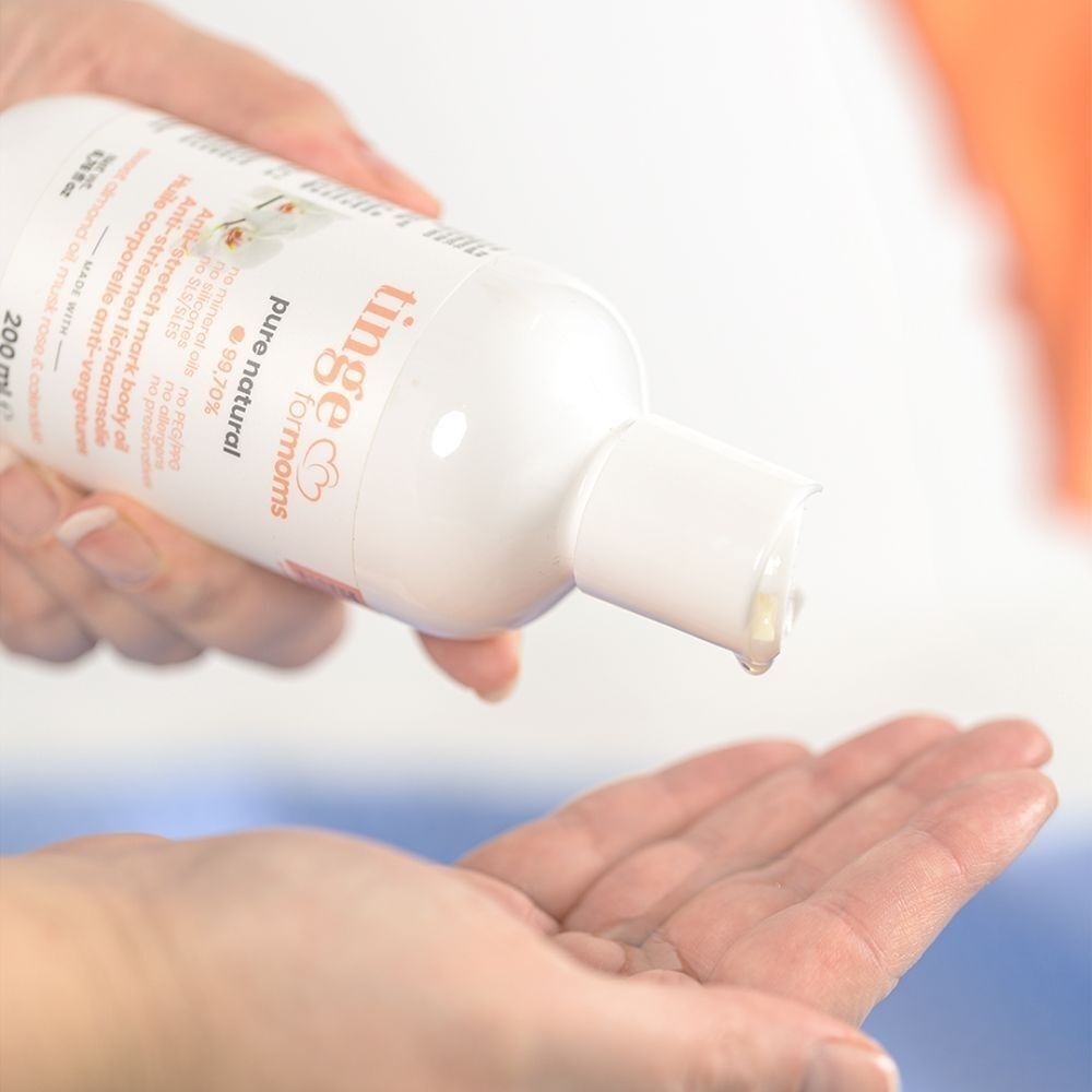 Een hand giet Tinge for Moms anti-striemen lichaamsolie in de andere hand.