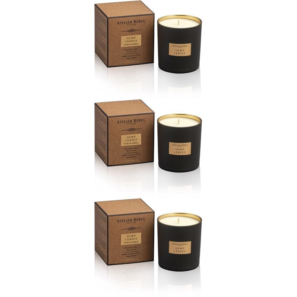 Bougie parfumée noire dans un verre à bord doré, à côté d'une boîte en carton marron.
