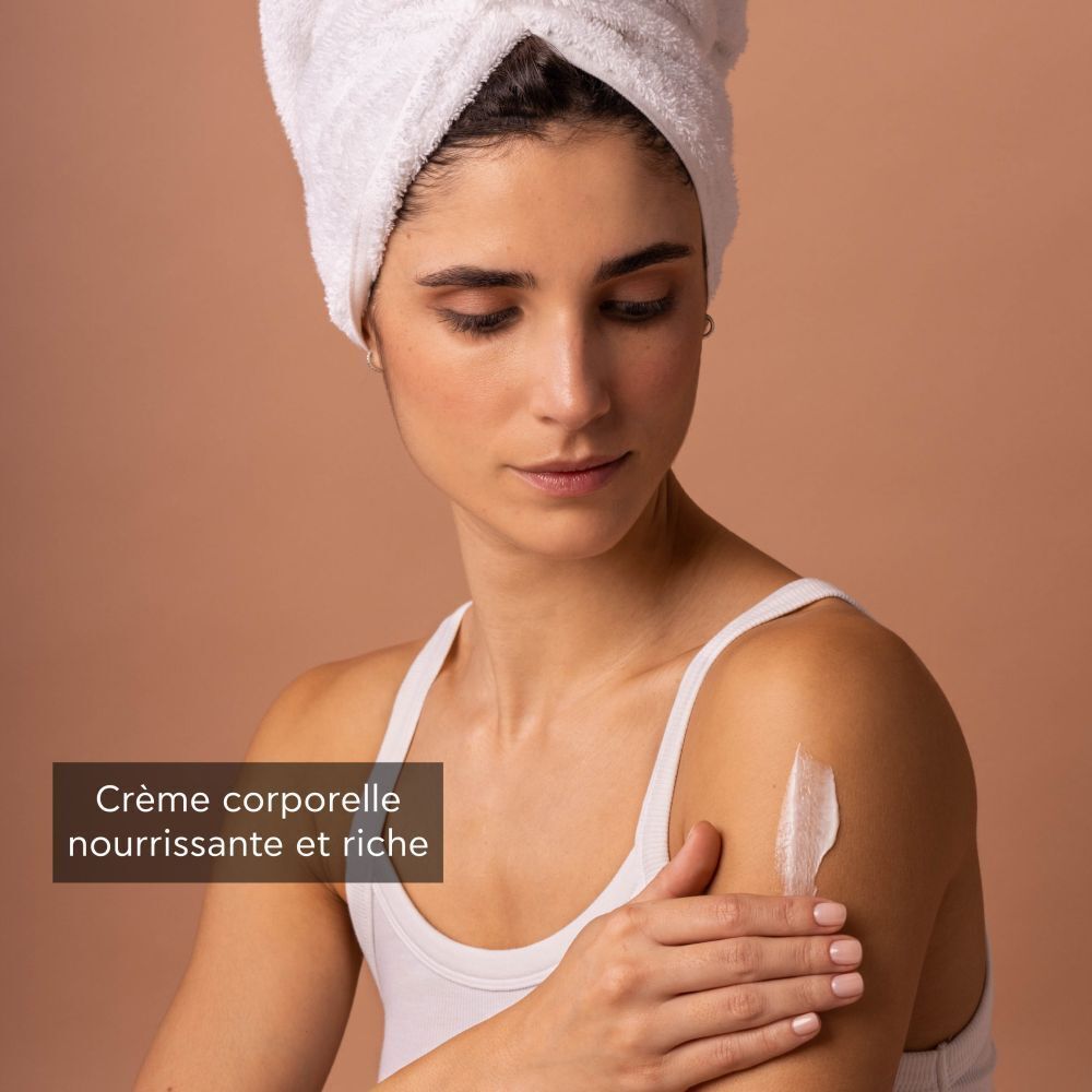 Femme avec une serviette sur la tête appliquant la crème corporelle Apivita Royal Honey.
