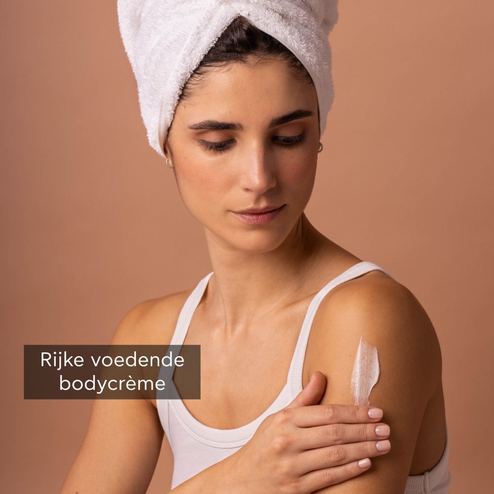 Vrouw met handdoek op hoofd brengt Apivita Royal Honey bodycrème aan op haar schouder.