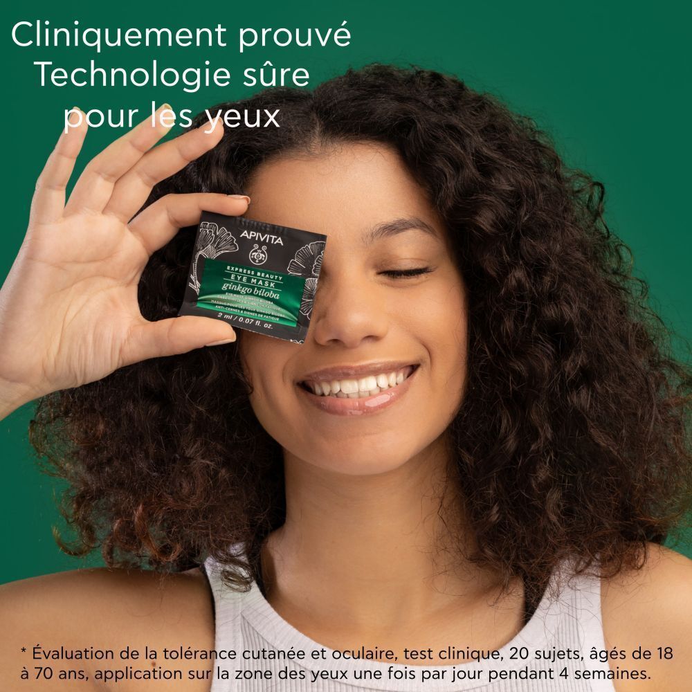 Femme tenant un sachet de Masque Yeux Apivita devant son œil.