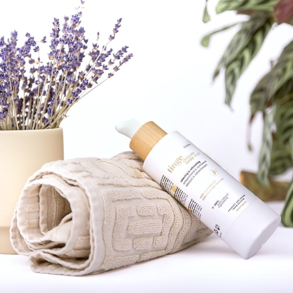 Fles Tinge Bodywash naast een handdoek en lavendel.