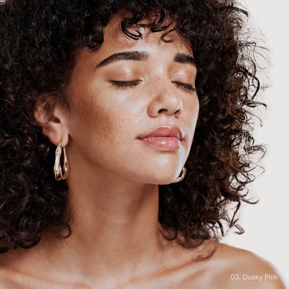 Vrouw met gesloten ogen en glanzende lippen, draagt Dusky Pink lip product.