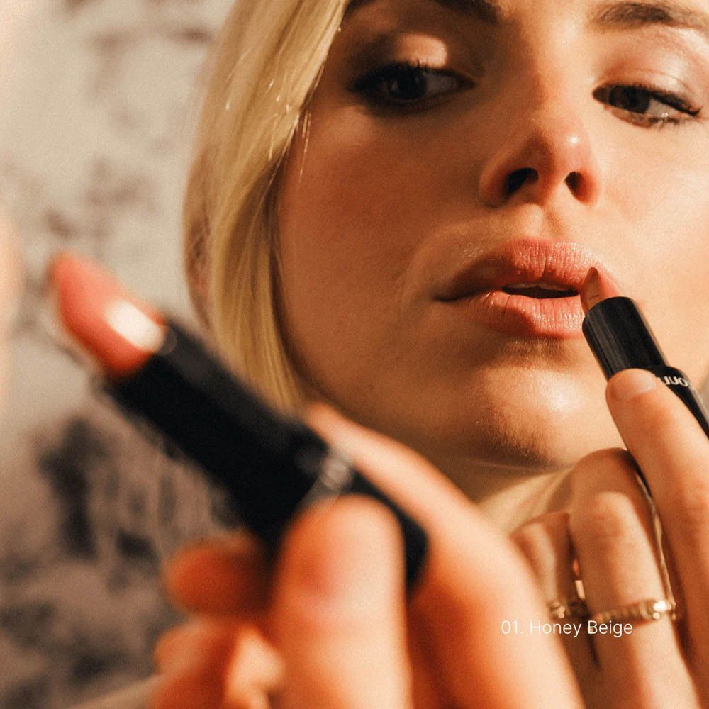 Une femme applique le rouge à lèvres 'Honey Beige'.