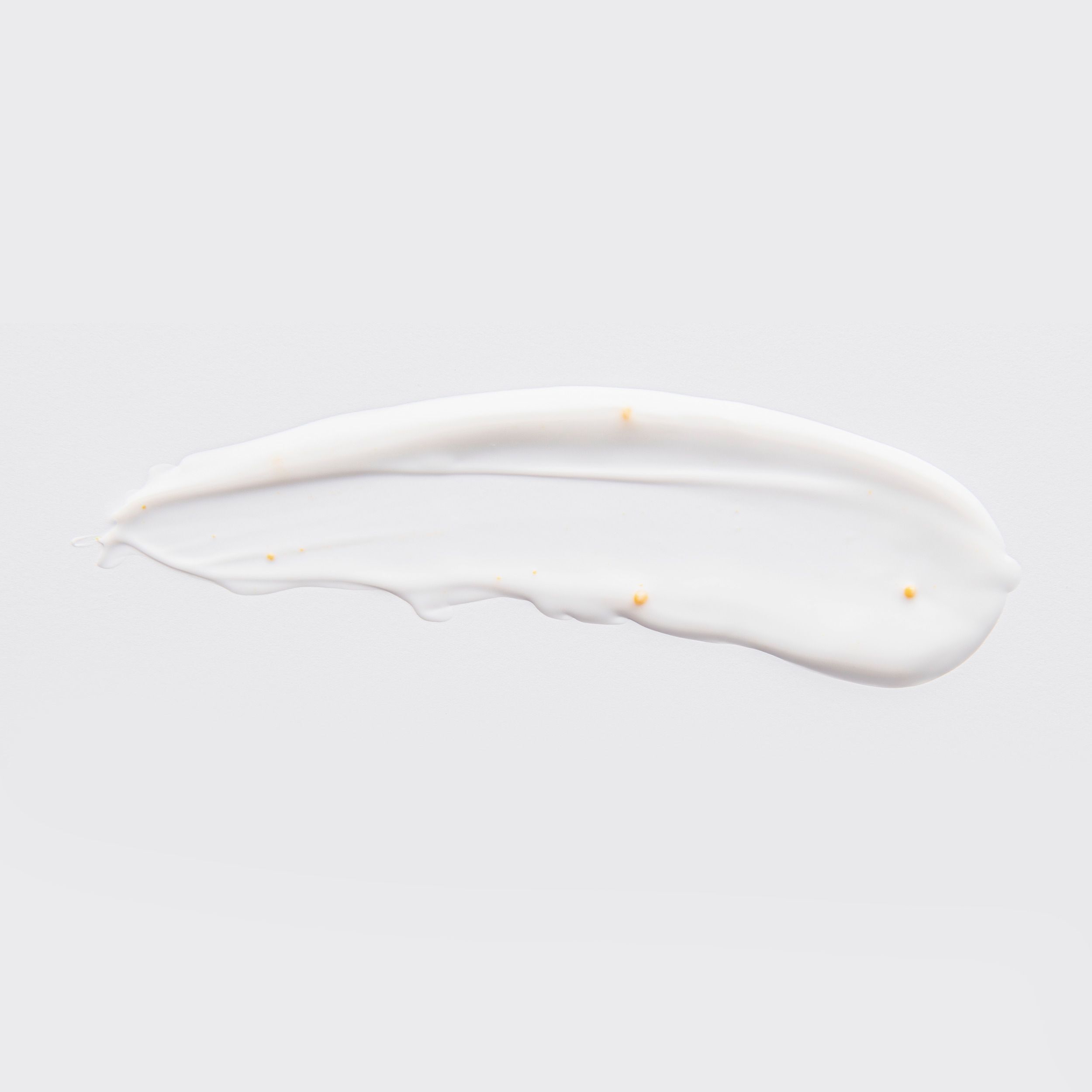 Een witte veeg bodycrème met kleine gouden parels op een lichte achtergrond.