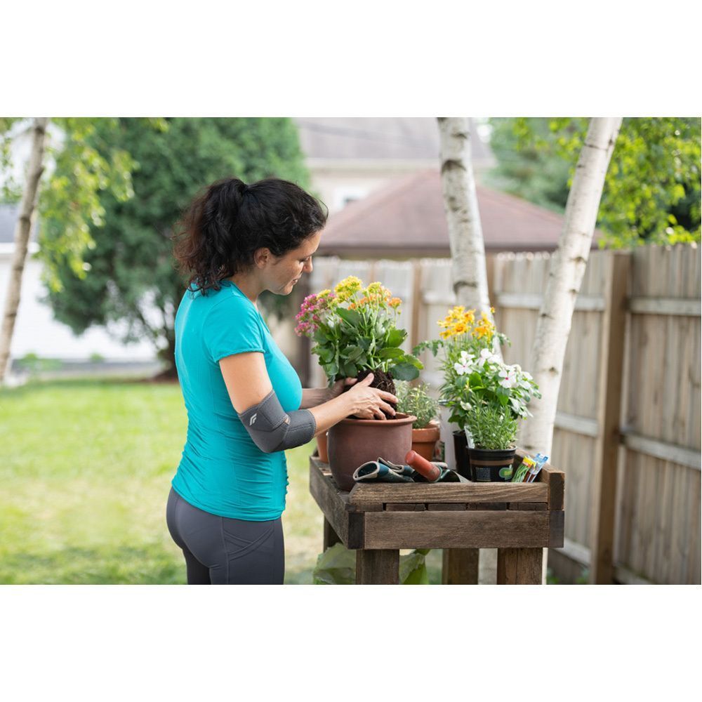 Femme portant un bandage de coude FUTURO Comfort Fit en train de rempoter des plantes dans le jardin.