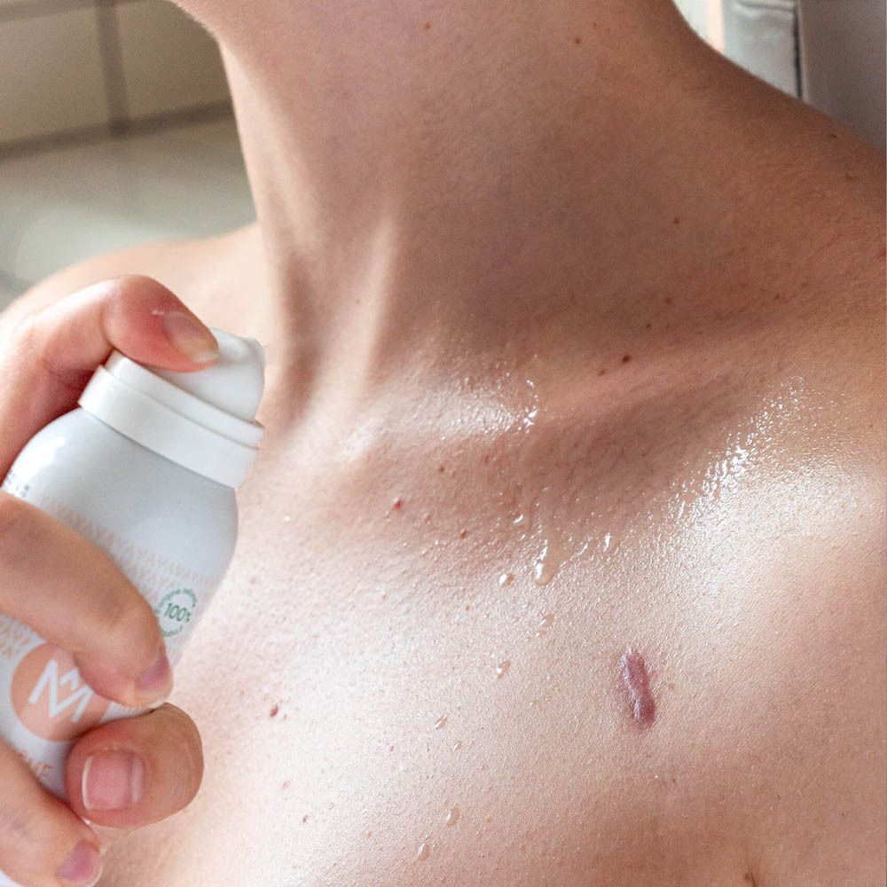 Une main pulvérise MÊME L'eau de soin sur la poitrine.