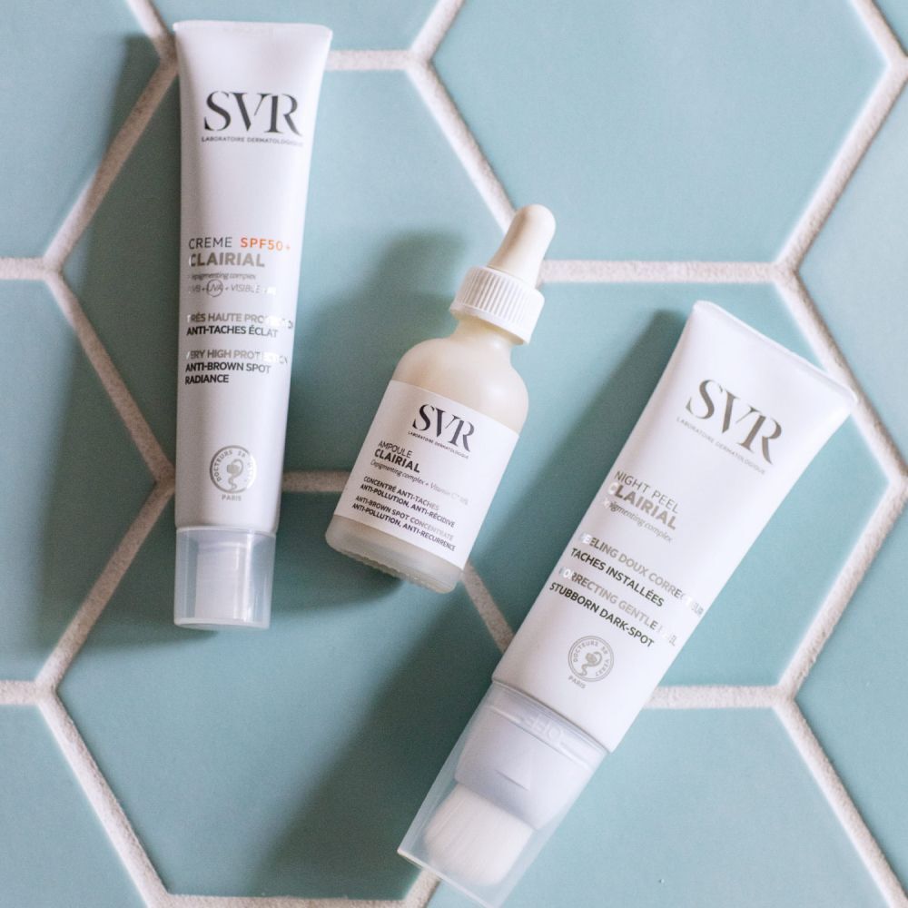 Flacon SVR Ampoule Clairial et deux tubes de crème sur fond carrelé.