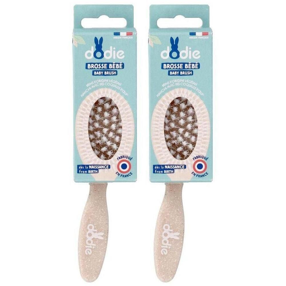 Deux brosses pour bébé Dodie en emballage carton. Les brosses ont un manche beige clair et une tête ovale avec des poils marron clair et blancs.