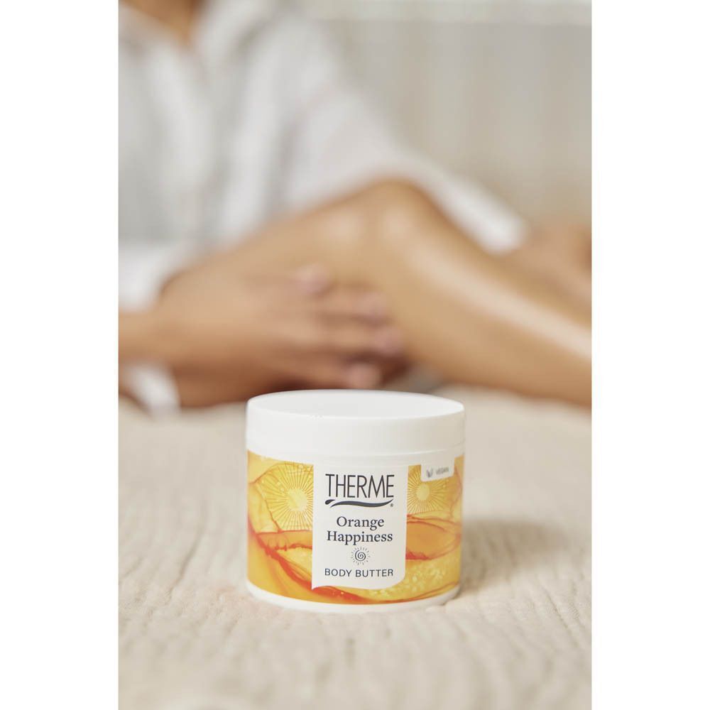 Een pot Therme Orange Happiness Body Butter op een bed, benen op de achtergrond.