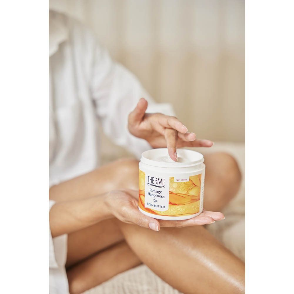 Une main prélève du Beurre Corporel Therme Orange Happiness d'un pot.