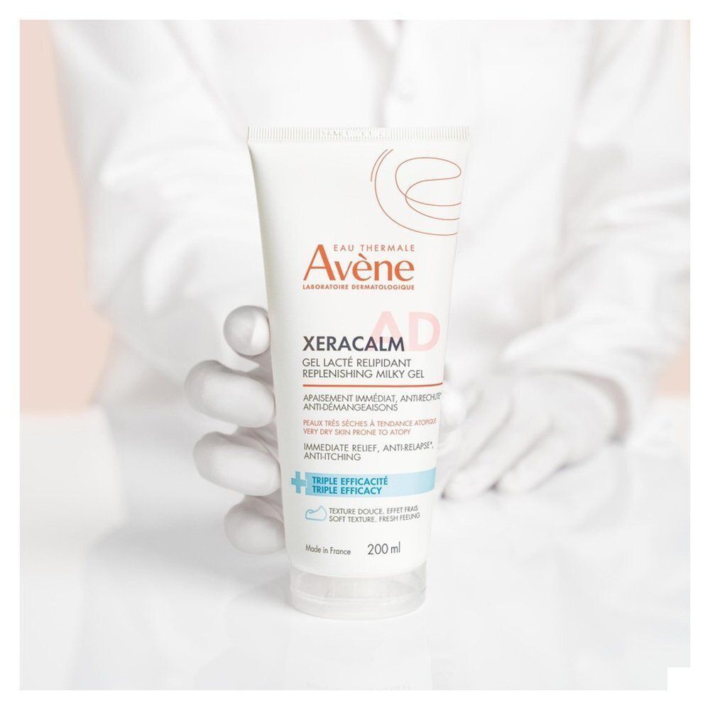 Een hand in een witte handschoen houdt een tube Avène XeraCalm AD Gel-Lait vast.
