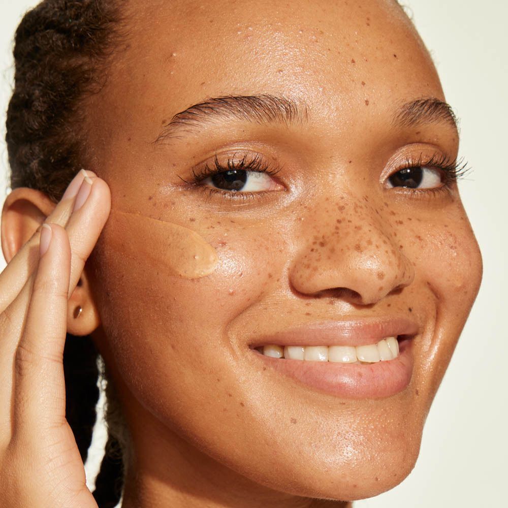 Une femme applique une crème hydratante bronzante sur sa joue.